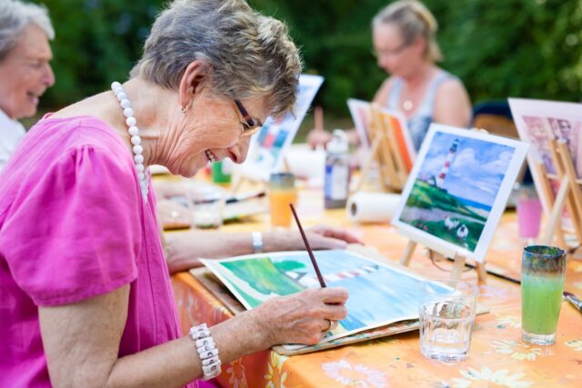 Elder LGBTQ woman painting outdoors with friends