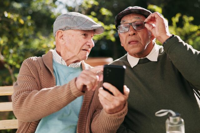 Two elder men sitting outside looking at cellphone