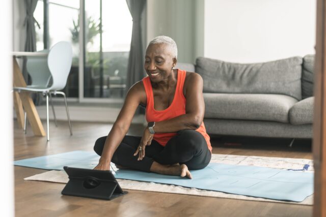 A person silting cross-legged on a yoga mat and looking at a tablet