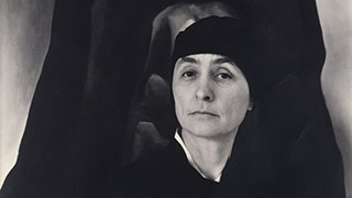 Black and white portrait of a woman wearing a dark headscarf, creating a serious and thoughtful expression.