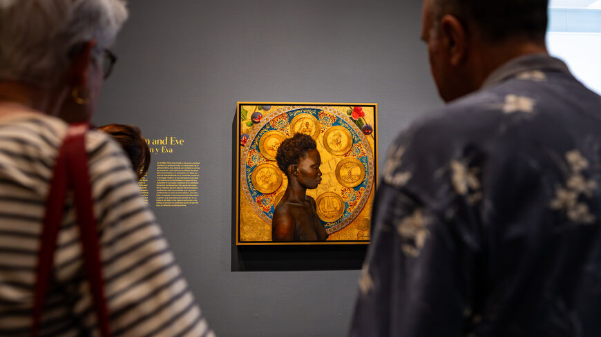 People viewing a framed painting in a gallery with focused lighting and a detailed background.