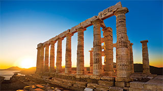 Ancient stone columns of the Temple of Poseidon at sunset, Sounion, Greece, with a clear blue sky in the background.