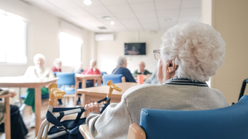 Elderly people sitting in a bright common room, engaging in conversation and activities at a senior care facility.