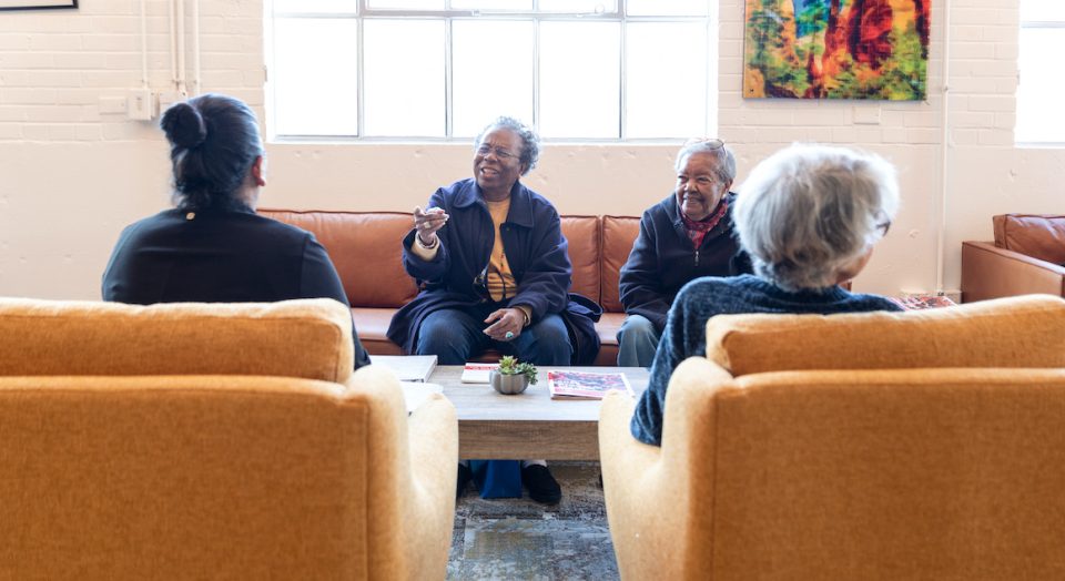 Four people sitting in a cozy living room, having a cheerful conversation with artwork on the wall.