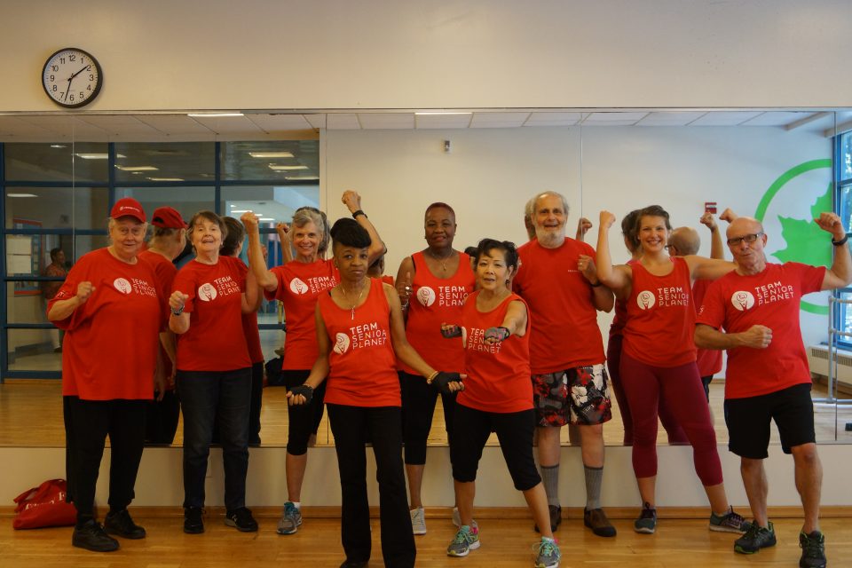 Group of people in red shirts posing energetically in a gym with mirrors, showing team spirit and unity.