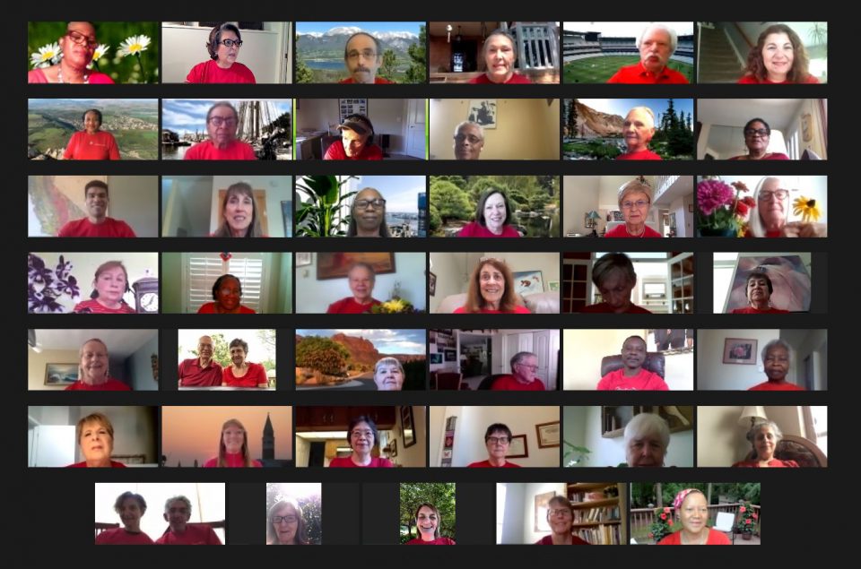 Virtual choir rehearsal with participants in red shirts on a video call grid.